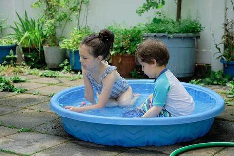 Siblings playing in a shallow pool in the backyard Stock Photos