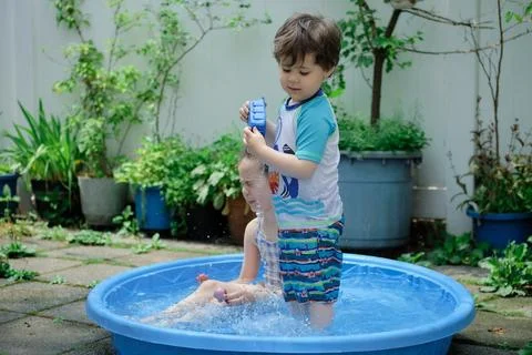 Siblings playing in a shallow pool in the backyard Stockfoto's