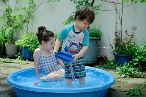 Siblings playing in a shallow pool in the backyard Stock Photos