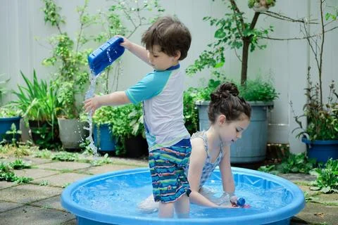 Siblings playing in a shallow pool in the backyard 库存照片