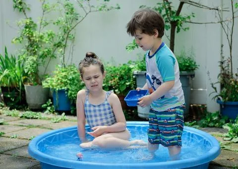 Siblings playing in a shallow pool in the backyard Stock Photos