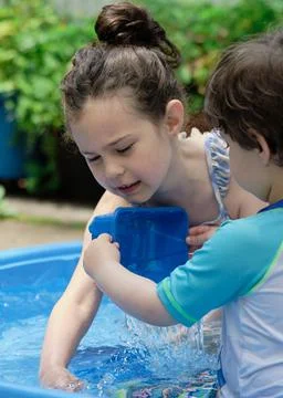 Siblings playing in a shallow pool in the backyard Stock Photos