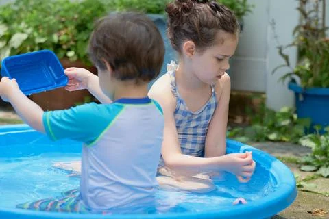 Siblings playing in a shallow pool in the backyard Stock Photos