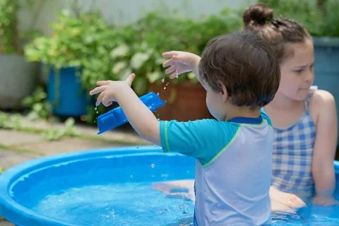 Siblings playing in a shallow pool in the backyard Stock Photos