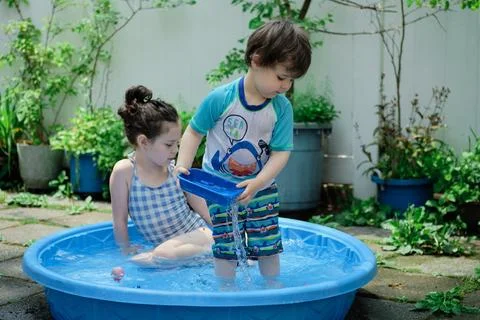 Siblings playing in a shallow pool in the backyard Stock Photos