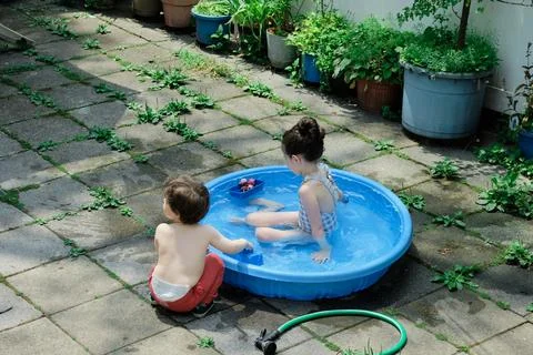 Siblings playing in a shallow pool in the backyard Stock Photos