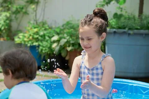 Siblings playing in a shallow pool in the backyard Stock Photos