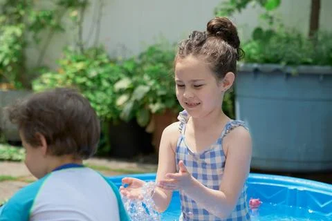 Siblings playing in a shallow pool in the backyard Stock Photos