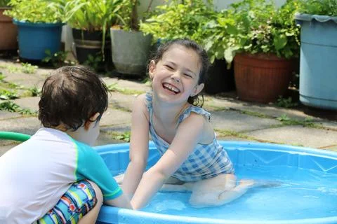 Siblings playing in a shallow pool in the backyard Stock Photos