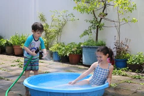 Siblings playing in a shallow pool in the backyard Fotos de archivo