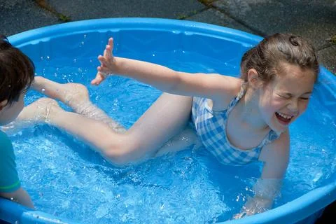 Siblings playing in a shallow pool in the backyard Stock Photos