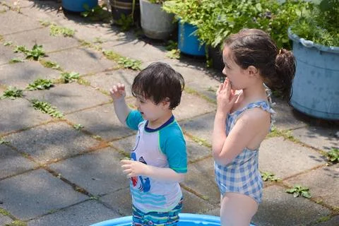 Siblings playing in a shallow pool in the backyard Stock Photos