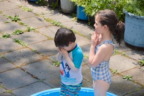 Siblings playing in a shallow pool in the backyard Stock Photos