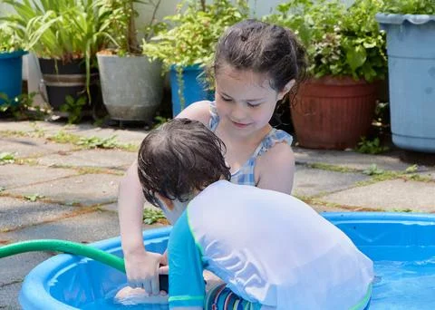 Siblings playing in a shallow pool in the backyard Stock Photos
