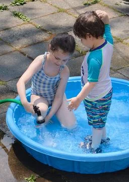 Siblings playing in a shallow pool in the backyard Stock Photos
