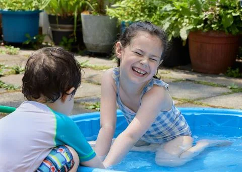Siblings playing in a shallow pool in the backyard Stock Photos