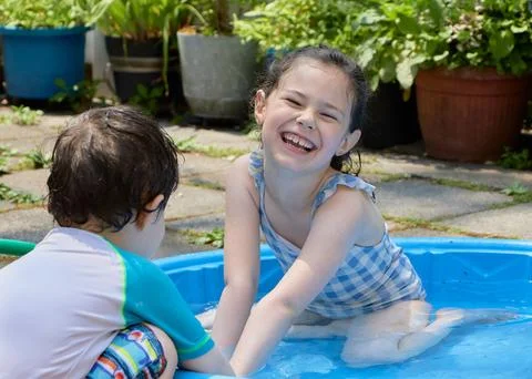 Siblings playing in a shallow pool in the backyard Stock Photos