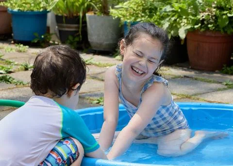 Siblings playing in a shallow pool in the backyard Stock Photos
