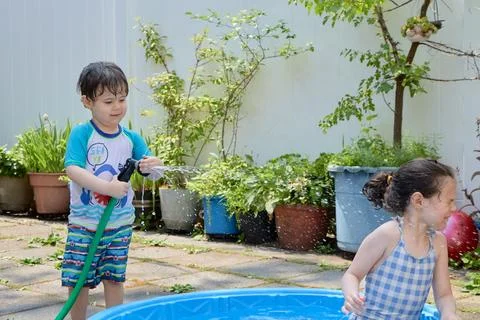 Siblings playing in a shallow pool in the backyard Stock Photos