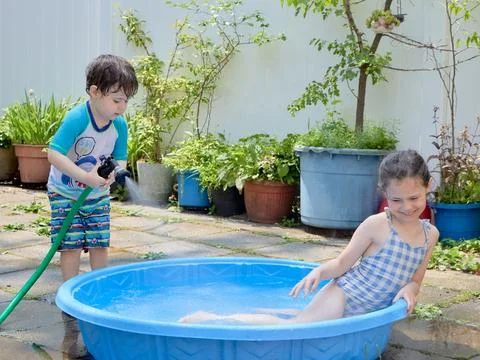 Siblings playing in a shallow pool in the backyard Stock Photos