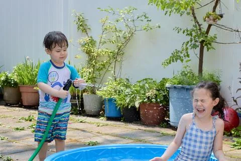 Siblings playing in a shallow pool in the backyard Stock Photos
