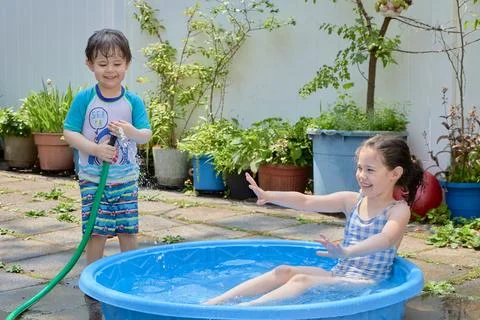 Siblings playing in a shallow pool in the backyard Stock Photos