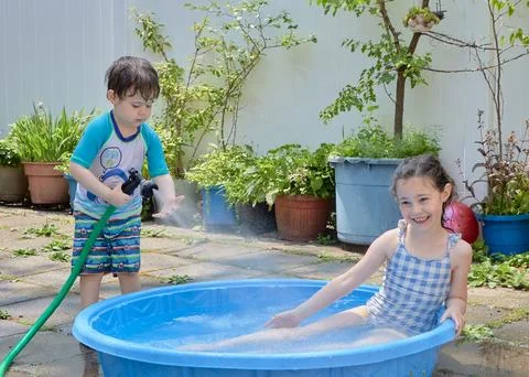 Siblings playing in a shallow pool in the backyard Stock Photos