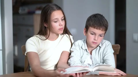 Siblings share a quiet reading session indoors. 動画素材 342771709