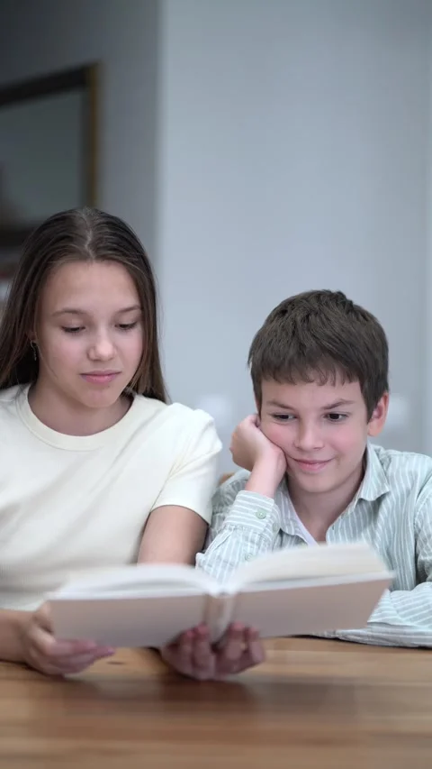 Siblings share a quiet reading session indoors. Stock-Footage 342771726