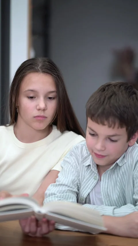 Siblings share a quiet reading session indoors. Vídeos de archivo 342771731