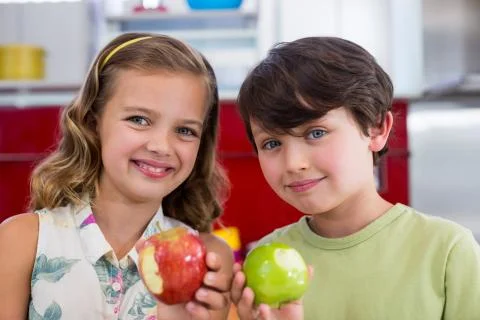 Siblings showing missing bite of apple in kitchen Stock Photos