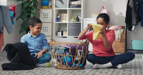 Siblings sit on the laundry room floor sorting colored clothes before putting Vídeo Stock 200002904