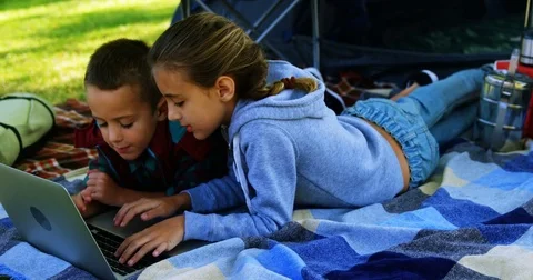 Siblings using laptop outside the tent at campsite Stock Footage