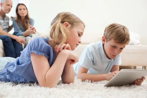 Siblings using a tablet computer with their parents on the background Stockfoto's