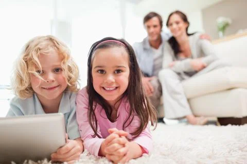 Siblings using a tablet computer while their parents are in the background Stock Photos