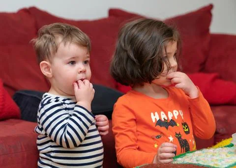 Siblings watching tv while eating grapes on Halloween Stock Photos
