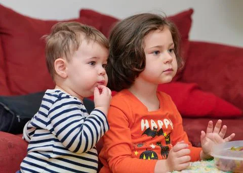 Siblings watching tv while eating grapes on Halloween Stock Photos