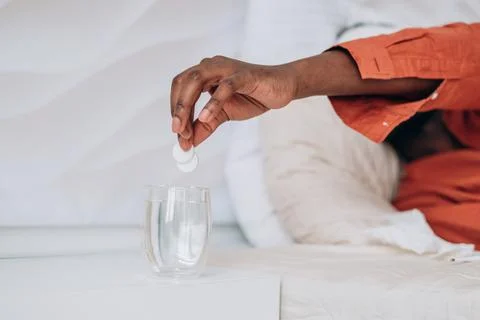 Sick African man throws two fever pills into a glass tumbler close-up Stock Photos