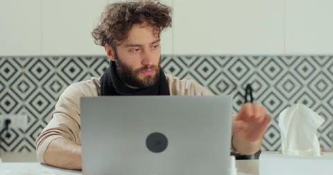 Sick bearded man blows his nose into a paper napkin while working remotely at Видео 168476697