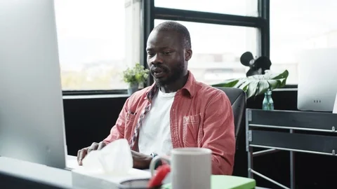 Sick black employee at desktop computer using paper tissues suffering virus Stock Footage 119330921