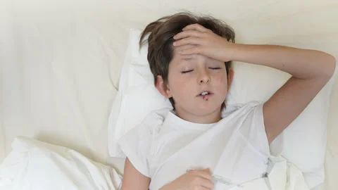 Sick boy with high fever lying on pillow in bed and holding thermometer. Tired Stock Footage 167911379