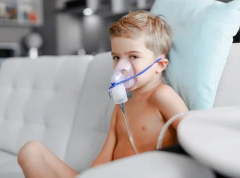 Sick boy in nebulizer mask making inhalation, respiratory procedure by pneumonia Stock Photos
