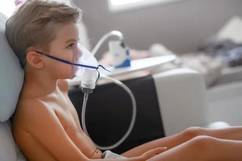 Sick boy in nebulizer mask making inhalation, respiratory procedure by pneumonia Stock Photos