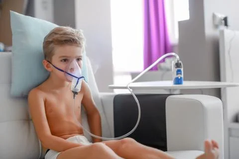 Sick boy in nebulizer mask making inhalation, respiratory procedure by pneumonia Stock Photos