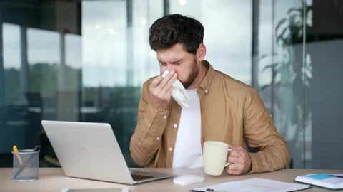 Sick businessman suffers from a cold while sitting at a desk at a workplace  Video stock 295042215