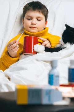 Sick child boy with digital thermometer in mouth lying in bed with fever illn Stock Photos