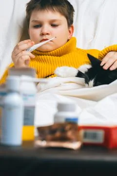 Sick child boy with digital thermometer in mouth lying in bed with fever illn Stock Photos