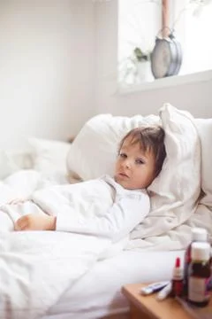 Sick child boy lying in bed with a fever Stock Photos