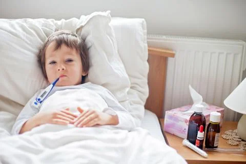 Sick child boy lying in bed with a fever Stock Photos