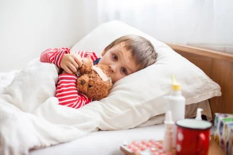 Sick child boy lying in bed with a fever, resting Stock Photos